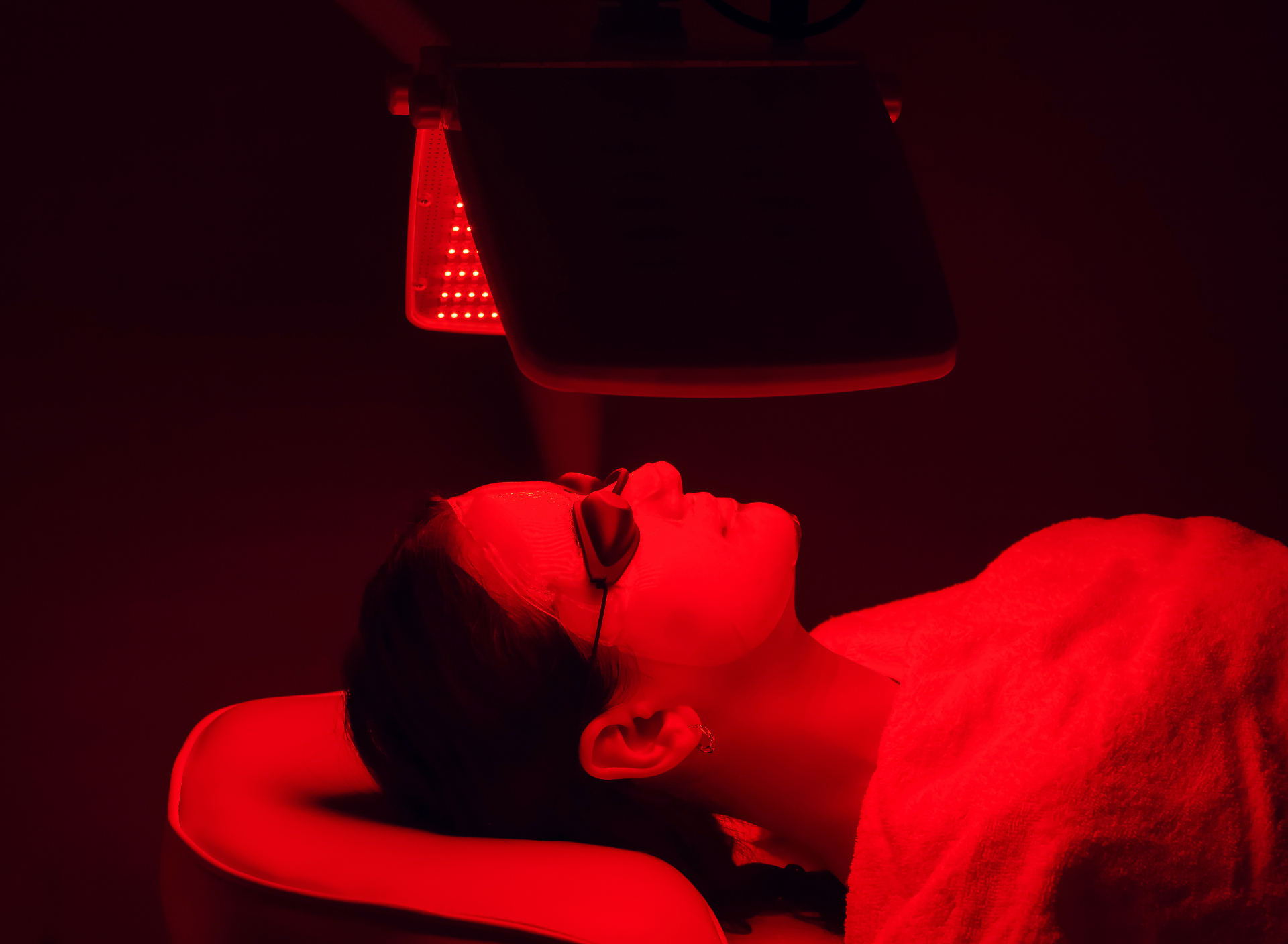 What to expect during a red light facial therapy session Woman receiving red light facial therapy with LED panel at REDSOL Wellness Club League City TX