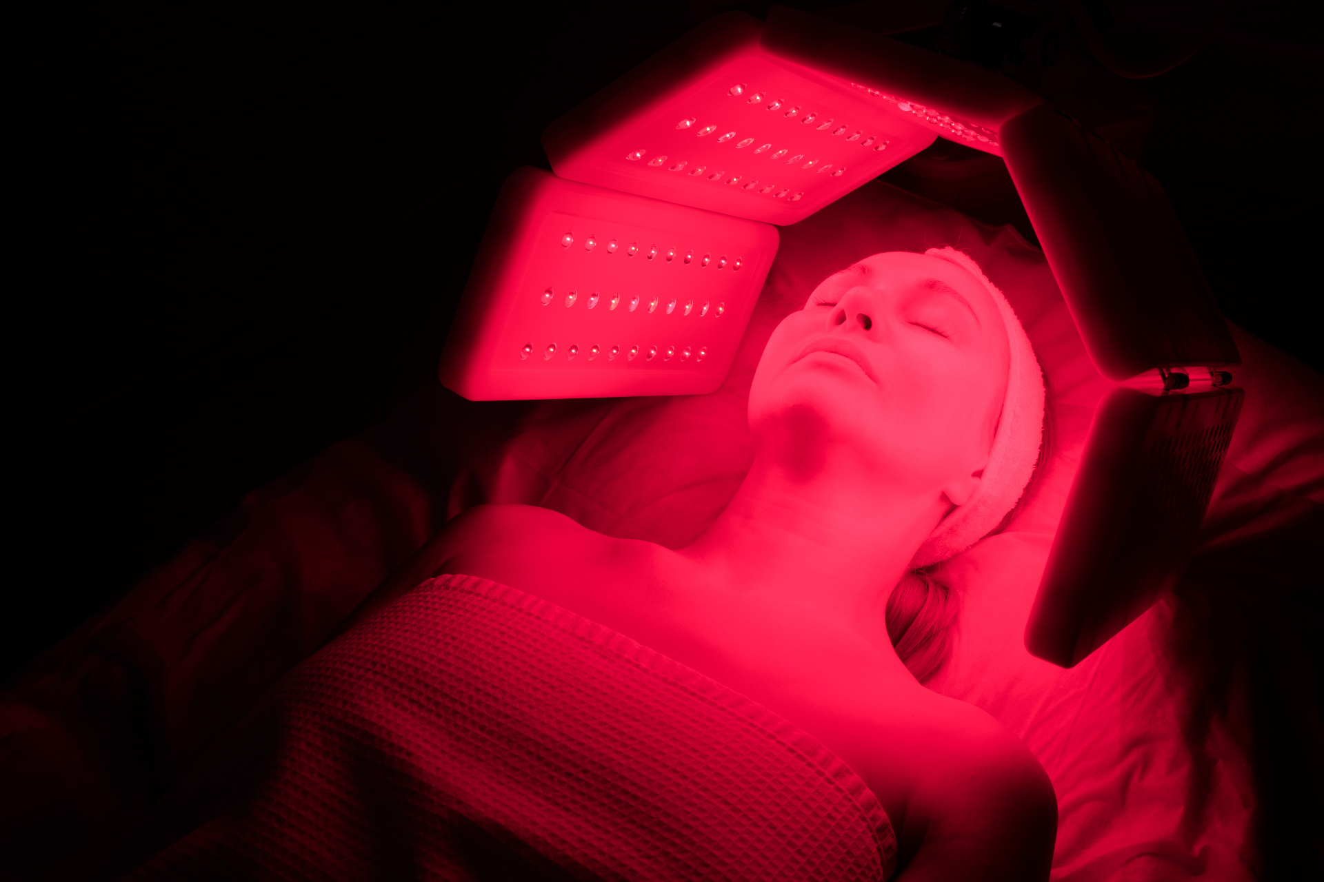 Red light facial LED therapy for wrinkle reduction and skin tone improvement Woman relaxing during red light facial treatment with multi-panel LED device for anti-aging at REDSOL Wellness Club